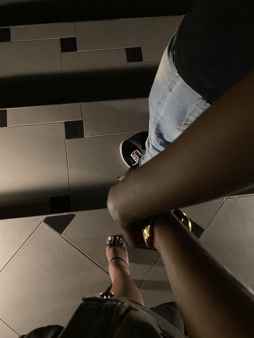 Two people stand together on a tiled floor, with one wearing light blue jeans and black Vans sneakers and the other in a black outfit with gold-accented heels, captured from a downward angle. The image complements the post's casual nightlife vibe, pairing the relaxed moment with the mention of "sleeping like babies" and the $RIVER tag from @RiverdotInc.
