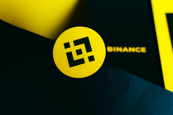 A close-up, 3D-rendered image of the yellow Binance cryptocurrency logo set against a dark background.