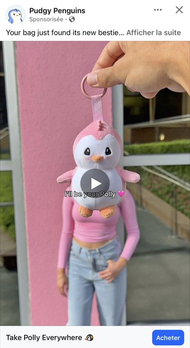 A sponsored Facebook advertisement from 'Pudgy Penguins' showing a hand holding a pink penguin keychain bag charm, with the caption 'Your bag just found its new bestie... Afficher la suite' and a blue 'Acheter' button labeled 'Take Polly Everywhere'.