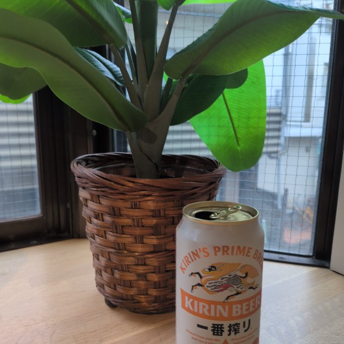 The image features a plant with large green leaves placed next to an open can of beer, specifically Kirin Beer. The beer can has a label that says "Kirin Beer" written in Japanese. The scene suggests that someone might be enjoying a drink while admiring their potted plant or simply relaxing at home.
