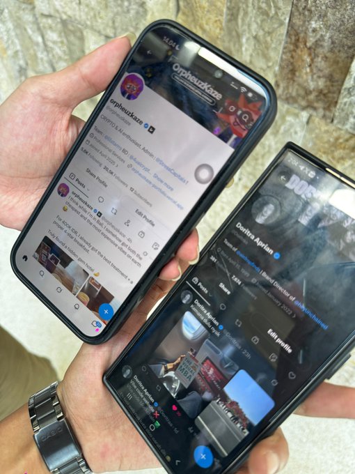 Two smartphones are held side by side, both displaying X (Twitter) profile pages with the usernames "OrpheusKuro" and "Doultro Ariel" visible on their screens.