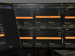 Multiple computer monitors displaying a dark interface containing lists, forms, or trading information.