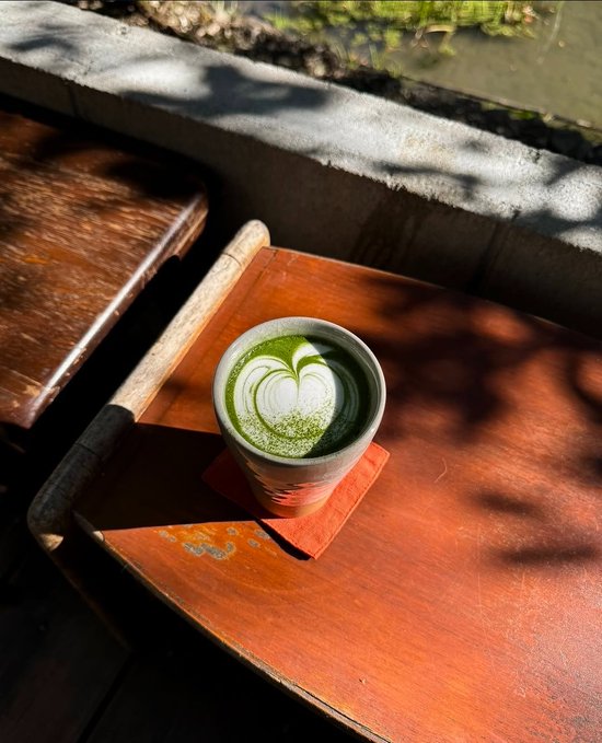 The image features a cup of green tea sitting on top of an orange coaster placed on a wooden table. The photo captures the details of the cup and its surroundings, including the coaster and the table. There are no texts or other objects present in the image, making it a simple yet visually appealing composition that highlights the cup of tea as the main subject.