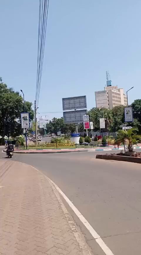 The image shows a street scene featuring a large building, a roundabout, and several people walking or riding motorcycles. The perspective of the photo suggests that it was taken from within the city streets, providing an up-close view of the urban environment. The caption provided by the image creator connects the scene to the post about decentralization in Kenya, which highlights how ADA funds are being used to support real students and their dreams.