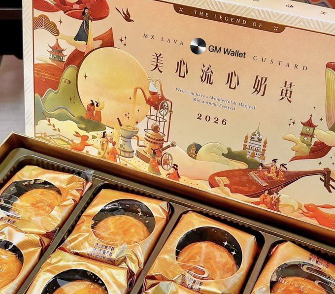 An open gift box of mooncakes titled 'THE LEGEND OF X', 'MX LAVA GM Wallet', and '美心流心奶黄' with the message 'Wish you have a Wonderful & Magical Mid-autumn Festival 2026'.