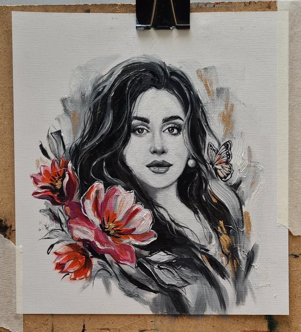The image shows a beautiful physical painting of a woman with dark, flowing hair rendered in black and white, accented with vibrant red and pink flowers and a delicate butterfly. A black binder clip secures the canvas to what appears to be a wooden board, fitting the "The Last Color" 15x15cm physical painting description shared in the post.