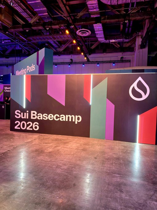 A photo of an event space featuring a colorful wall with the text 'Sui Basecamp 2026' and the Sui logo, alongside a 'Meeting Pods' sign in the background.