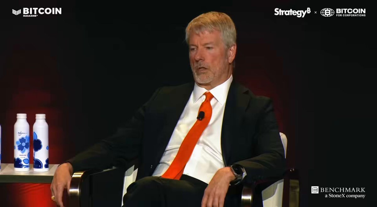 The image features a man wearing an orange tie sitting in a chair with his arms crossed while looking off into the distance. The background of the image shows two bottles, one blue and one white, placed next to each other. The text "strategy" is also visible in the image.
