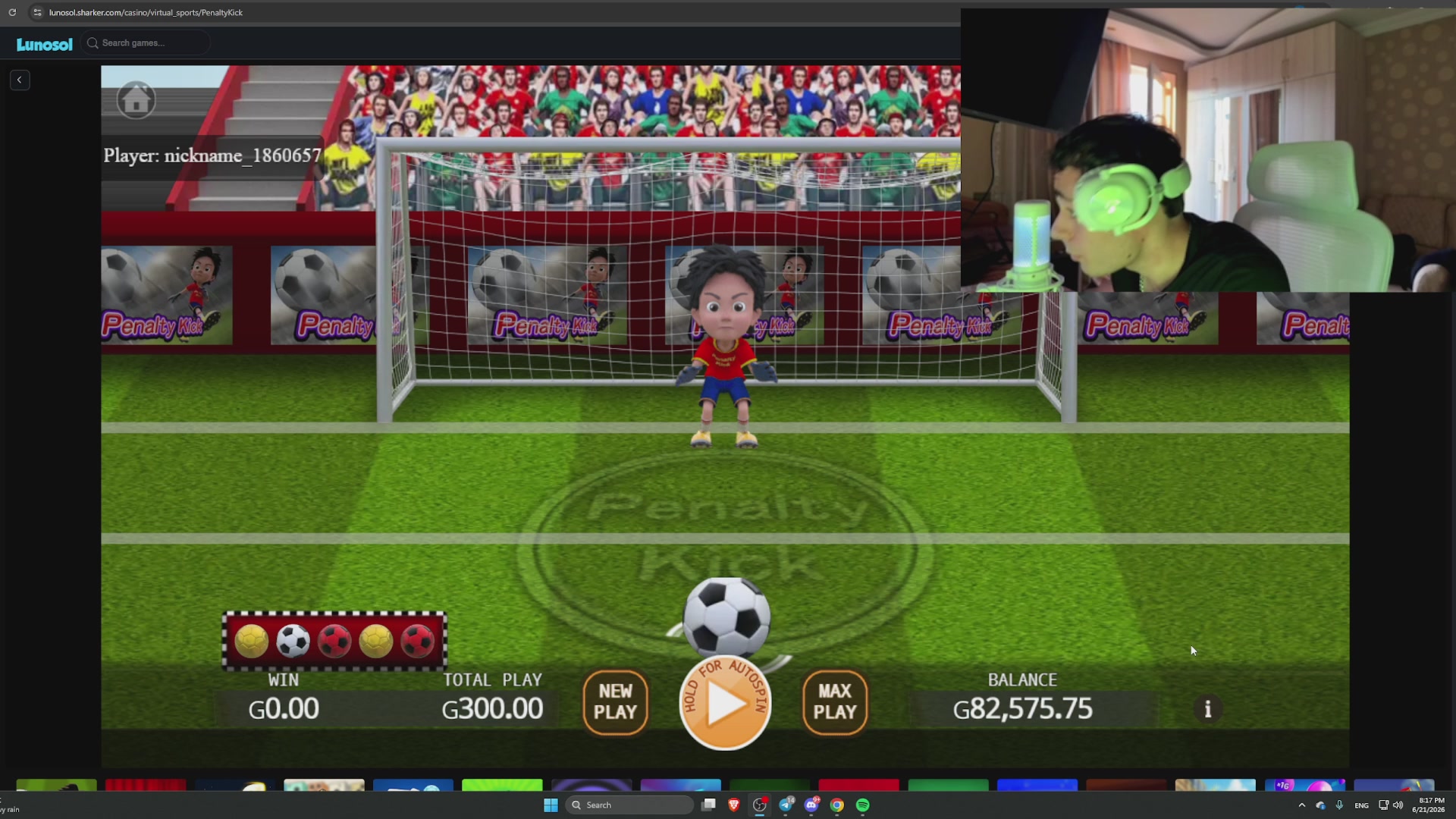 The image shows a man playing a video game with a soccer ball displayed on his screen. The background of the image features a soccer field with players positioned around the goal area. There are also several other people visible in the scene, possibly watching or waiting for their turn to play. The main focus is on the man and the soccer ball, which he is interacting with while playing the game.