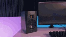 The image shows an electronic device, possibly a computer or sound system, placed on top of a desk with a monitor behind it. The background appears to be a dark room, which contrasts with the brightly lit foreground. A keyboard can also be seen in front of the device. The caption at the bottom of the image reads "May on Decibel was a Banger".