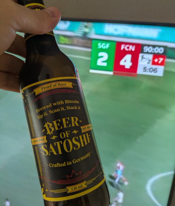 A hand holds a bottle of "Beer of Satoshi" (330ml, crafted in Germany, "Proof of Beer" edition) in front of a TV showing the final score of an SGF vs. FCN match ending 2-4 at 90:00, celebrating the 1. FC Nürnberg derby victory.