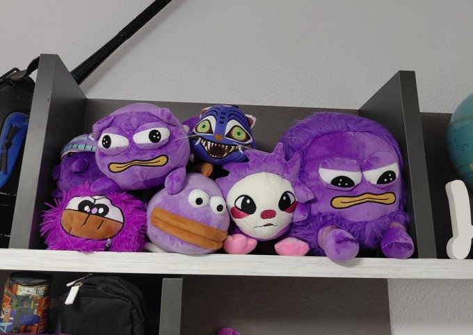 A wooden shelf displaying a collection of plush toys, mostly featuring characters with purple bodies, including what appears to be characters from Five Nights at Freddy's.