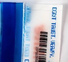 A close-up of a package with a barcode and text reading 'DON'T TRUST, VERIFY,' alongside a blue item with 'I NEED THIS' printed on it.