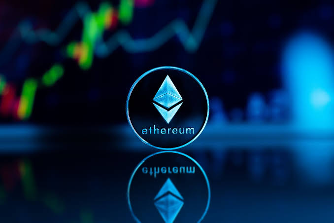 A glowing blue Ethereum logo is prominently displayed in front of a blurred candlestick price chart, with its reflection visible on the surface below. The image visually represents the post's news of a crypto whale accumulating additional ETH.