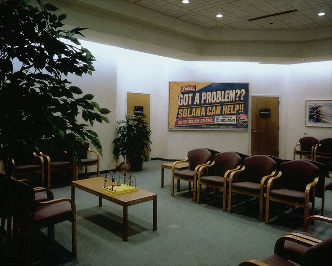 An empty waiting room features rows of chairs, a coffee table with a puzzle, plants, and a wall poster reading 'Falken GOT A PROBLEM?? SOLANA CAN HELP!! ANY SIZE, HIGH SPEED, GUM WRAPPERS, SOLANA'.