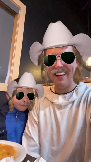 A selfie of two people wearing matching cowboy hats and aviator sunglasses, with their faces partially obscured by cartoon cowboy hat and mustache stickers.