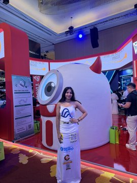 A woman poses in front of a large mascot character display at what appears to be a corporate or trade show event.