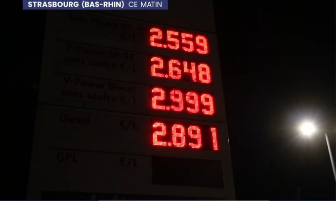A nighttime photo from Strasbourg (Bas-Rhin) shows a digital gas station price board displaying V-Power 95 at 2.559€, V-Power 98 at 2.648€, V-Power Diesel at 2.999€, and Diesel at 2.891€.
