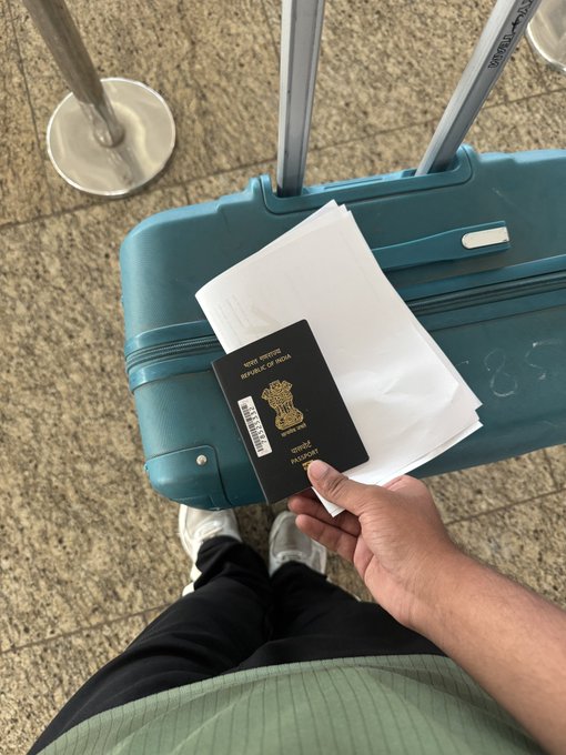 A traveler holds an Indian passport ("REPUBLIC OF INDIA") and boarding passes atop a teal suitcase in an airport terminal, capturing the moment of departure to Tokyo.