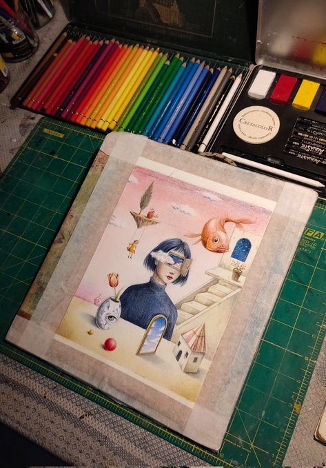The image features a painting of a woman with a fish head, surrounded by various colored pencils and markers. The painting is placed on top of a green table or board, which has been wrapped in paper for protection during the creative process. The artist's work is displayed prominently, showcasing their talent and dedication to their craft.