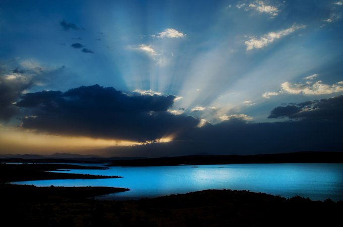 A serene lake glows with reflected blue light beneath a dramatic sky, where sunbeams pierce through dark clouds at sunset.

The image perfectly captures the "Water Wednesday" theme, showcasing a tranquil body of water as the focal point, with its luminous blue surface mirroring the moody, sunlit sky above—inviting viewers to share their own water-themed visuals.