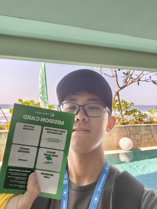 A young man wearing glasses, a black cap, and an "Xendit" lanyard holds up a Tokopedia "Mission Card" at what appears to be Villa Beach Horizon, with a pool and ocean visible in the background, supporting his post about completing Day 2 of his mission with a distribution partner.