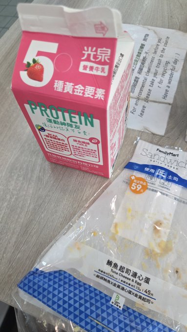 A pink and white carton of Kuang Chuan (光泉) strawberry-flavored protein milk next to a FamilyMart Sandywich package of Tuna Cheese & Egg.