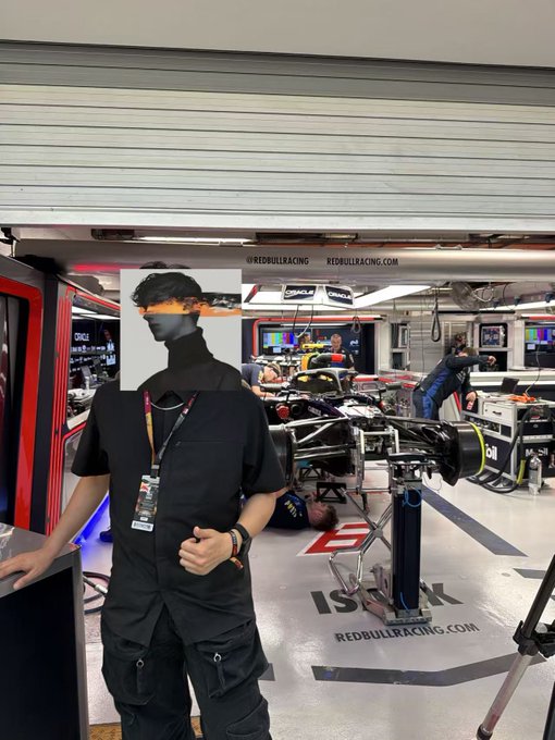 A team member in black stands in the Red Bull Racing garage, with "REDBULLRACING.COM" prominently displayed on the wall and floor, alongside a large Formula 1 car and equipment being worked on by crew members in the background. The image captures the post's theme of being at the Red Bull garage with a collaborator, surrounded by the team environment and machinery that metaphorically parallels the trading journey of gains, pullbacks, and forward momentum.