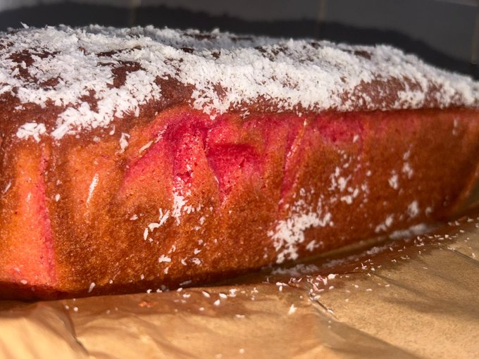 Close-up of a bundt-style cake dusted with powdered sugar, showing pink and red layers on the cut side, resting on parchment paper.