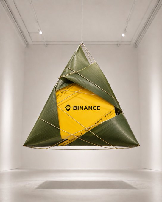 ikebana art piece made of green leaves, tied together with a yellow rope, hanging from the ceiling. The art piece has a Binance Dragon Boat Festival logo at its center.