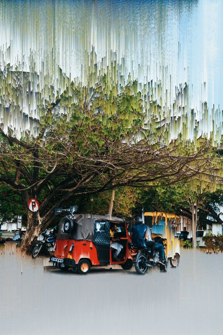 The image shows several vehicles, including an orange four-wheeler parked next to a tree, a motorcycle, and two bicycles. The car has a black stripe across its side. In addition, there are multiple people present in the scene, with one person standing near the bike and three others scattered throughout. They appear to be engaged in conversation or simply enjoying their time outdoors.