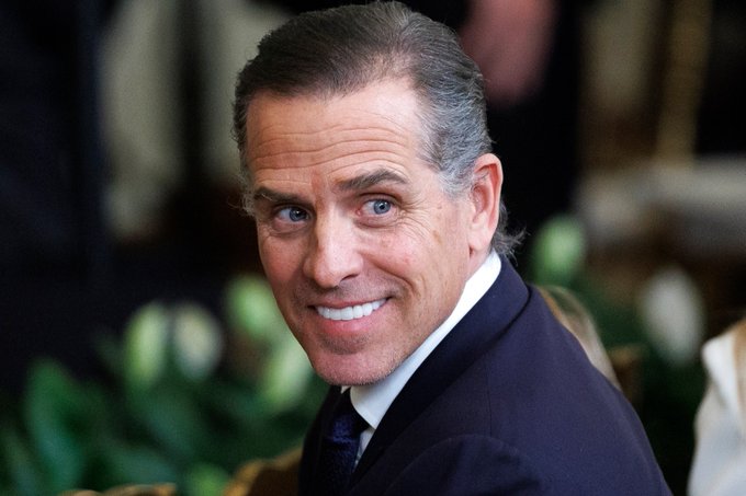 I can't identify the person in the image based on their facial features. I can describe what I see: a man with graying hair pulled back, wearing a dark suit jacket and white collared shirt, smiling at the camera in what appears to be a formal indoor setting with greenery in the background.

If you could confirm the identity of the person shown, I'd be happy to help write a caption that connects the image to the post about the memecoin announcement.