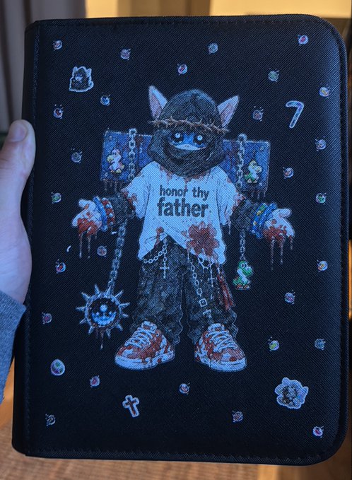 A black tablet case features a cartoon cat in a crown and chains, wearing a shirt that says “honor thy father,” surrounded by small icons including a cross and the number “7.”