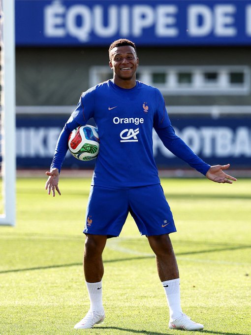 The image features a soccer player wearing an orange jersey, standing on a field with his arms outstretched. He holds a soccer ball in one hand while wearing white socks. The background of the photo shows a stadium or sports field, indicating that this is likely taking place during a soccer match or training session. The post also contains text related to soccer and football, suggesting that it might be promoting a specific event or team.