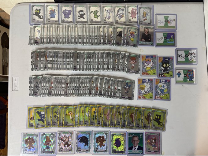 A collection of trading cards, likely Pokémon-themed, arranged in rows on a white surface, including stacks of silver-bordered cards and character cards along the bottom.