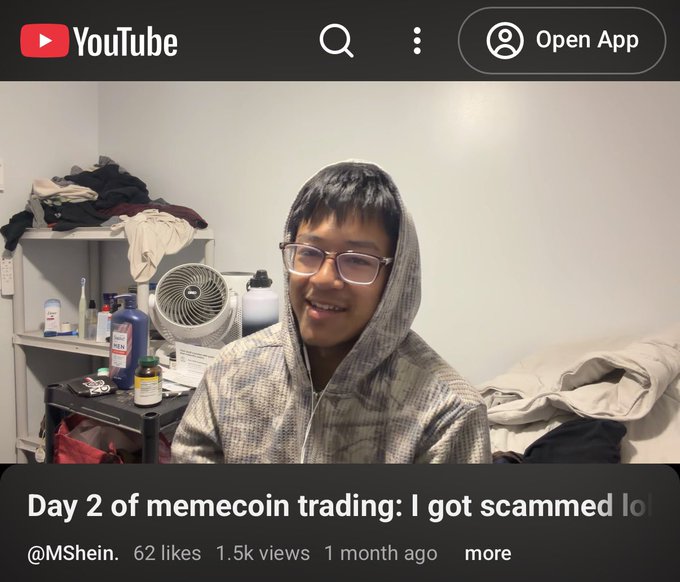 A YouTube thumbnail showing a smiling young man in a grey checkered hoodie, with the title "Day 2 of memecoin trading: I got scammed lol" posted by @MShein.