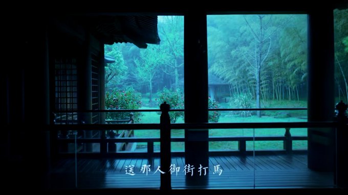 A dark, atmospheric view from inside a traditional Japanese-style wooden structure looking out onto a misty garden with bamboo and greenery, with Chinese subtitles reading '送那人御街打馬' at the bottom.