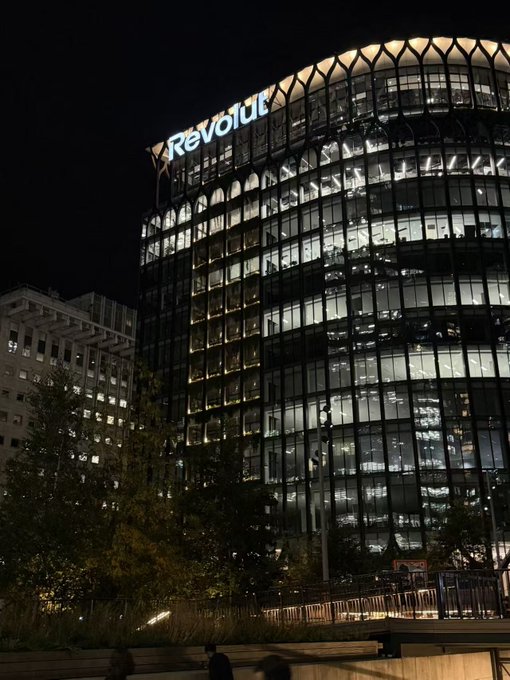 The illuminated "Revolut" sign crowns the modern, curved glass facade of the company's Canary Wharf office in London at night, where a customer visited seeking help with approximately $28,000 in restricted funds.