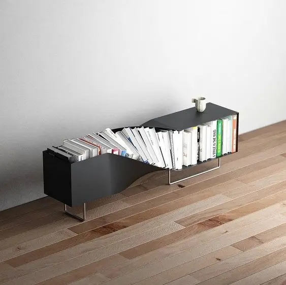 A modern black bookshelf with a distinctive curved/twisted design holds a collection of white-spined books and a small white vase, displayed on a wooden floor.
