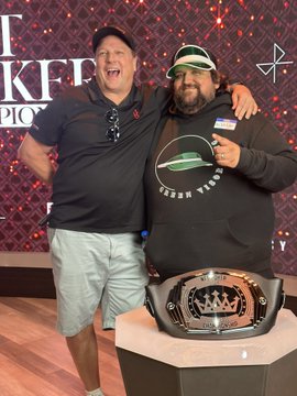 Two men posing together at a 'UFO Taco' event, one wearing a black 'UFO TACO' hoodie, standing behind a championship-style belt featuring a UFO logo on a pedestal.