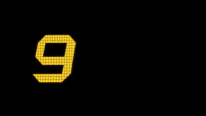 A digital number 9 made of yellow illuminated square segments, displayed on a black background resembling a train station or airport display board.