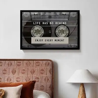 A framed black-and-white art print of a cassette tape with the text 'LIFE HAS NO REWIND' and 'ENJOY EVERY MOMENT' hangs above a pink headboard.