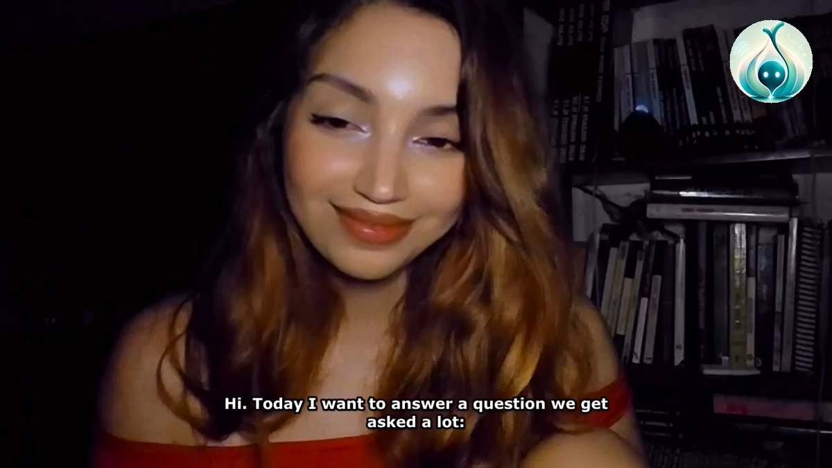 A young woman with long wavy auburn hair, wearing a red off-shoulder top, smiles at the camera with subtitles reading "Hi. Today I want to answer a question we get asked a lot:" and a circular green logo appears in the upper right, suggesting the image is a thumbnail or screenshot from a Q&A video related to the crypto token $Garly.