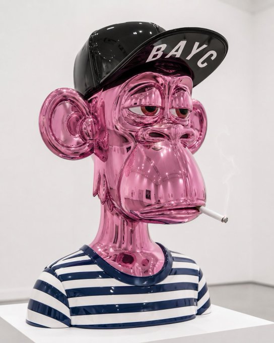 A glossy pink Bored Ape Yacht Club (BAYC) NFT sculpture displayed in a gallery, wearing a black cap with 'BAYC' lettering, smoking a cigarette, and dressed in a blue and white striped shirt.