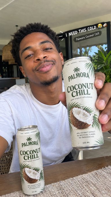 A young man poses with two cans of "PALMORA COCONUT CHILL" beverage (330 ML), with a caption overlay reading "I NEED THIS COLD 😮‍💨🥥" along with "Palmora Coconut Chill".