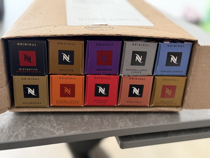 A cardboard box containing an assortment of Nespresso Original line coffee capsules, including Ristretto, Volluto, Arpeggio, Buenos Aires Lungo, Tokyo Lungo, Nicaragua, Vienna Lungo, Capricci, and Odacio varieties.