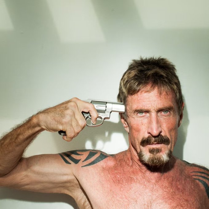 A shirtless, bearded man with tribal tattoos holds a silver revolver to the side of his head, staring intensely into the camera.
