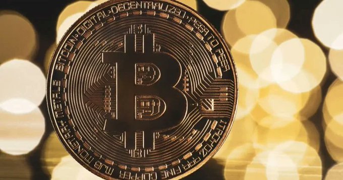 A close-up of a physical Bitcoin coin with gold bokeh lighting in the background.