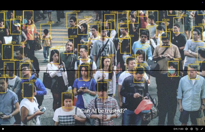 A crowd of people overlaid with yellow facial recognition bounding boxes and tracking IDs, captioned with the question 'Can AI be trusted?'