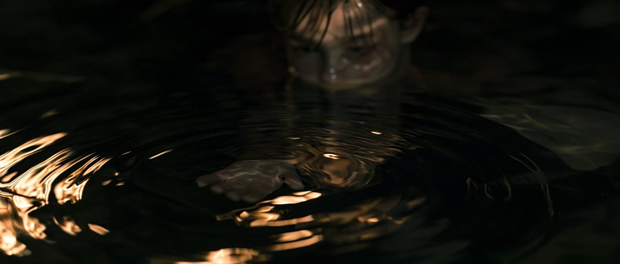 A young boy is submerged up to his nose in dark water, his outstretched hand creating ripples with shimmering light reflections. The moody image visualizes the feeling of "burning" resources and diving deep into work, mirroring the exhaustion and dedication of churning through hundreds of thousands of credits on multiple AI projects simultaneously.